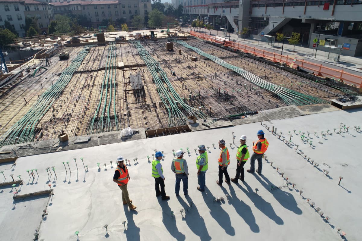 Construction workers observing rebar placement on a large paving area.